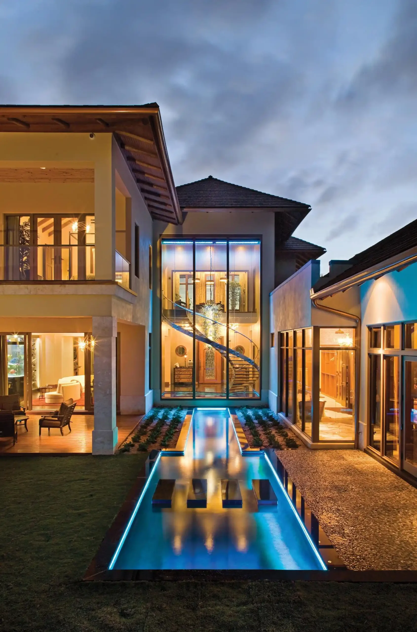 Modern villa with glass facade, elegant lighting, and reflective pool at sunset