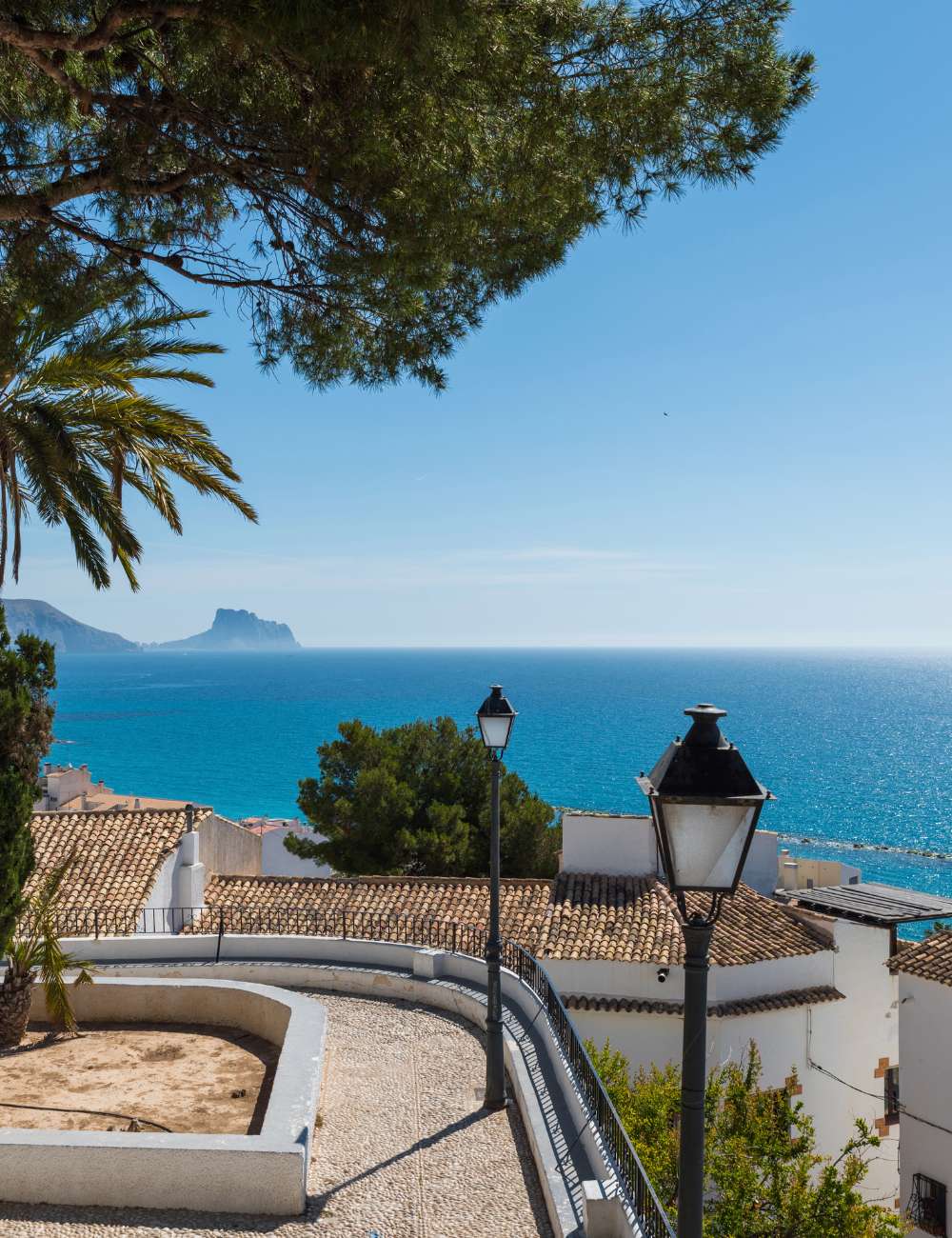 View of the Mediterranean Sea framed by palm trees and traditional lamp posts in Altea